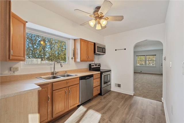 kitchen with ceiling fan, appliances with stainless steel finishes, sink, and light hardwood / wood-style flooring