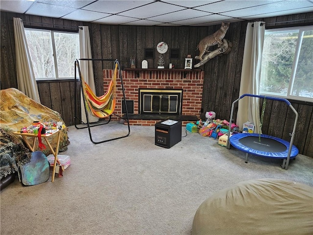 recreation room featuring carpet, a drop ceiling, wooden walls, and a fireplace