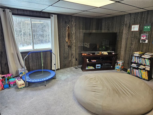 living area with carpet flooring, a paneled ceiling, and wood walls