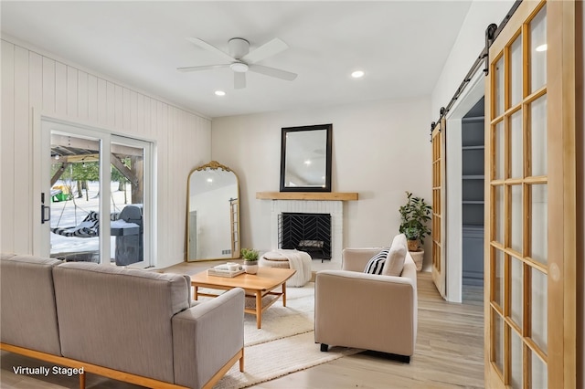 living area featuring light wood-style flooring, a barn door, recessed lighting, ceiling fan, and a fireplace