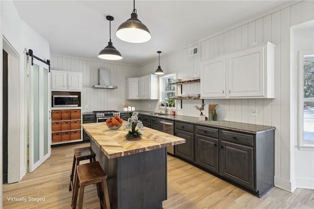 kitchen with a sink, visible vents, white cabinetry, wall chimney range hood, and wood counters