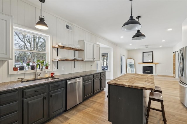 kitchen with stainless steel appliances, light wood-style flooring, a sink, open shelves, and wood counters