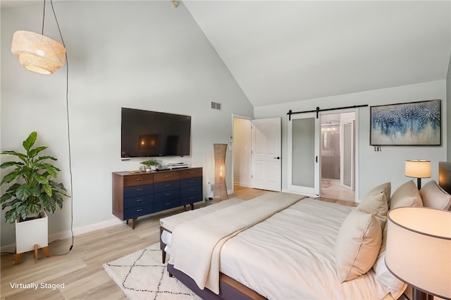 bedroom with light wood finished floors, a barn door, baseboards, visible vents, and high vaulted ceiling