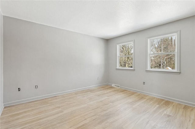 empty room with light wood-style flooring, visible vents, and baseboards