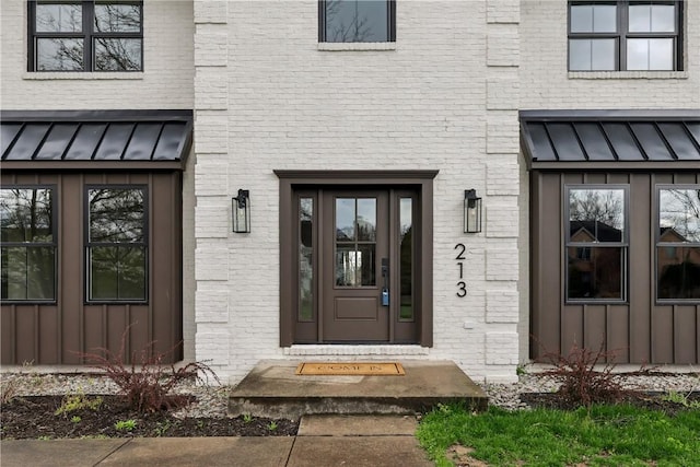 doorway to property with brick siding, a standing seam roof, board and batten siding, and metal roof