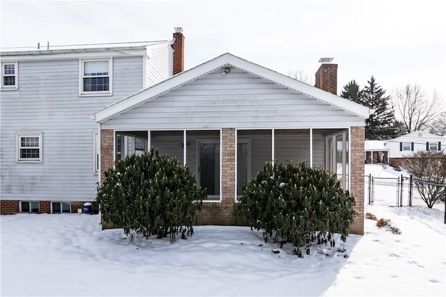 snow covered rear of property with a sunroom