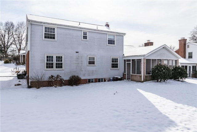 snow covered back of property featuring a sunroom