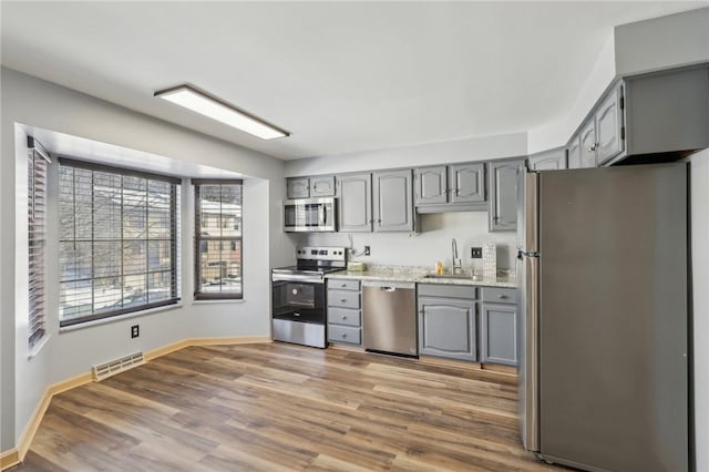 kitchen with sink, gray cabinetry, stainless steel appliances, light stone counters, and dark hardwood / wood-style flooring