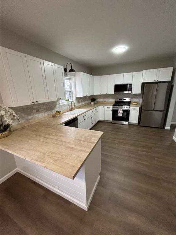 kitchen featuring white cabinetry, sink, kitchen peninsula, stainless steel appliances, and dark wood-type flooring