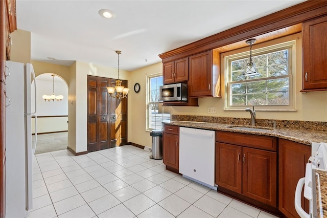 kitchen featuring sink, white appliances, light tile patterned floors, hanging light fixtures, and light stone countertops