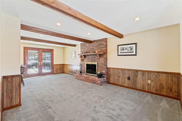 unfurnished living room with a brick fireplace, light carpet, beam ceiling, and french doors