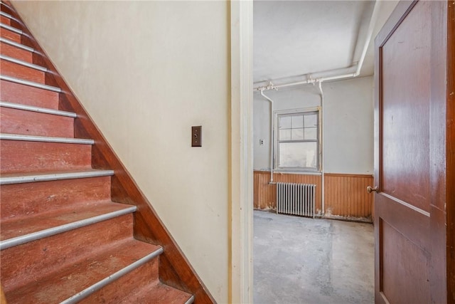 staircase featuring concrete flooring, radiator heating unit, and wooden walls