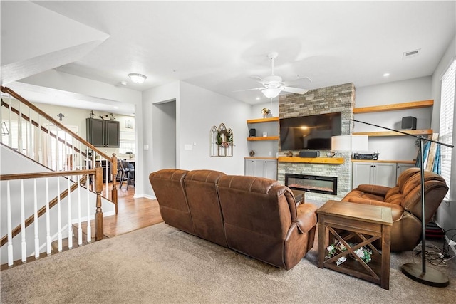 living room featuring ceiling fan, light colored carpet, and a stone fireplace