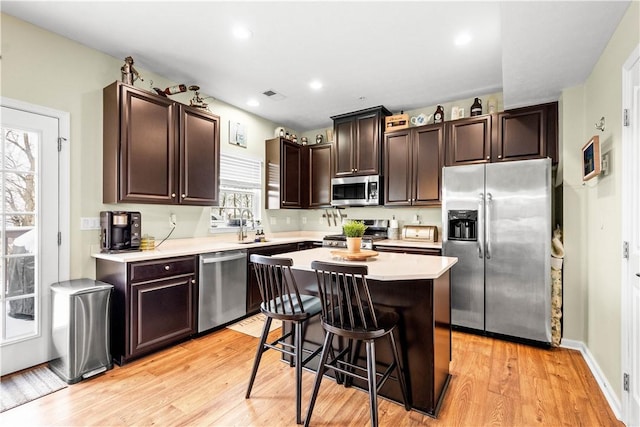 kitchen featuring a kitchen island, a kitchen bar, stainless steel appliances, a healthy amount of sunlight, and light wood-type flooring