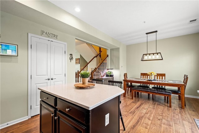 kitchen featuring a breakfast bar, a center island, dark brown cabinets, hanging light fixtures, and light hardwood / wood-style floors