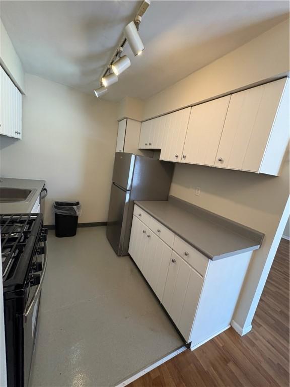 kitchen with sink, dark wood-type flooring, track lighting, range with gas stovetop, and white cabinets