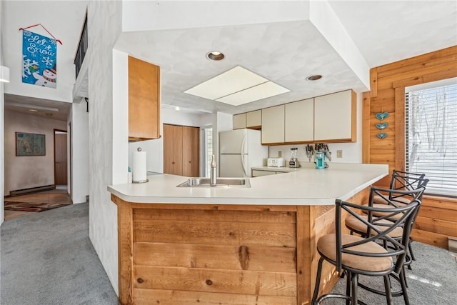 kitchen with sink, light carpet, wooden walls, kitchen peninsula, and white fridge