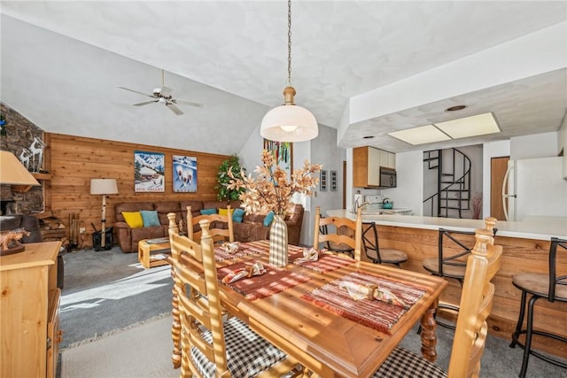 dining area featuring ceiling fan, lofted ceiling, light carpet, and wood walls