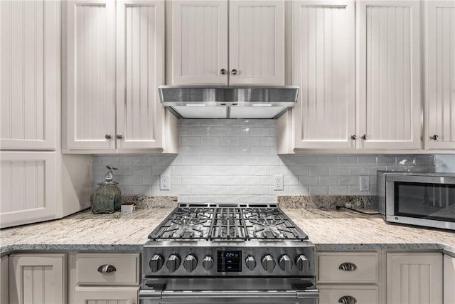 kitchen featuring light stone counters, white cabinetry, stainless steel appliances, and backsplash