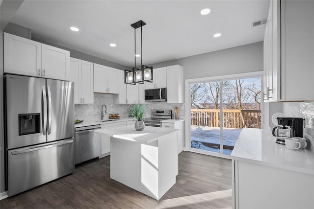 kitchen with dark wood-type flooring, appliances with stainless steel finishes, white cabinetry, hanging light fixtures, and a center island