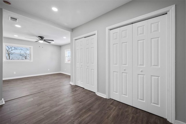 unfurnished bedroom featuring multiple closets, ceiling fan, and dark hardwood / wood-style flooring