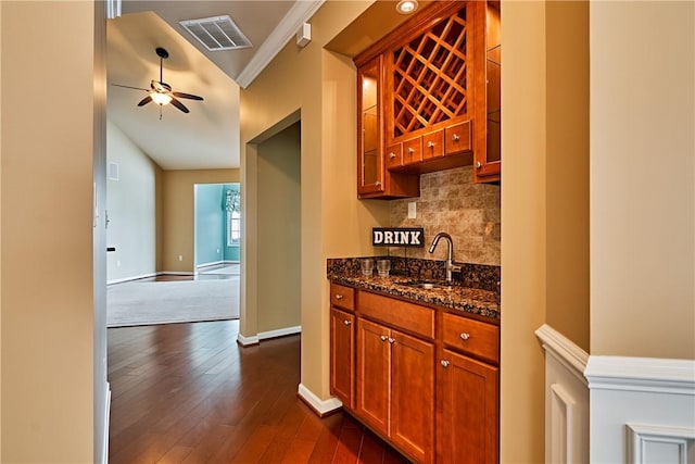 bar featuring sink, dark wood-type flooring, ceiling fan, dark stone countertops, and ornamental molding