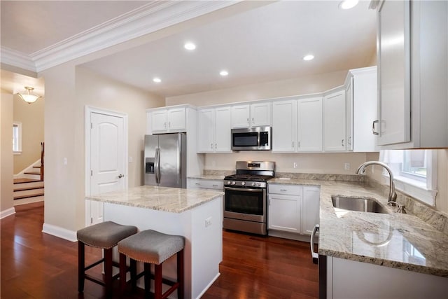 kitchen with appliances with stainless steel finishes, sink, white cabinets, a center island, and light stone counters