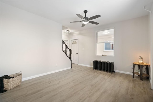 unfurnished living room featuring ceiling fan, radiator heating unit, and light hardwood / wood-style flooring