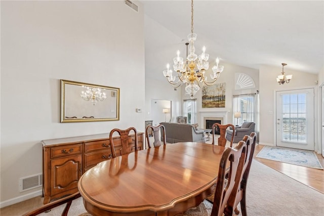 dining space with a notable chandelier, light hardwood / wood-style flooring, and high vaulted ceiling