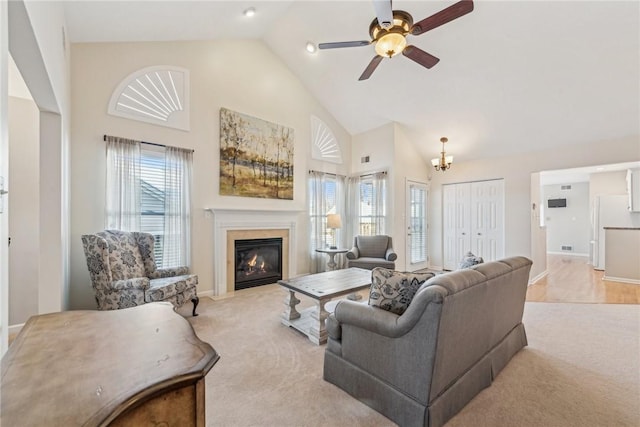 carpeted living room with ceiling fan with notable chandelier, plenty of natural light, and high vaulted ceiling