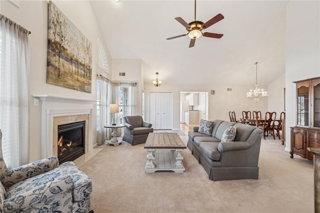 carpeted living room with ceiling fan with notable chandelier, high vaulted ceiling, and a tile fireplace