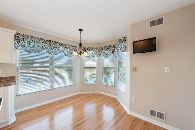 unfurnished dining area with a chandelier and light hardwood / wood-style flooring