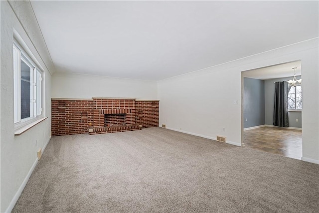 unfurnished living room with an inviting chandelier, a fireplace, and carpet flooring