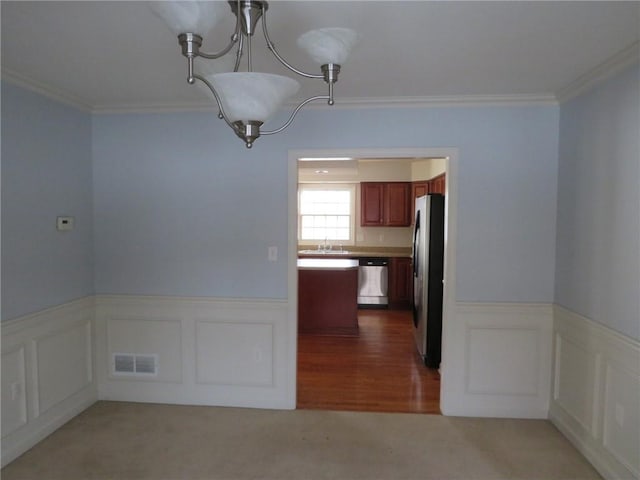 unfurnished dining area with ornamental molding, sink, light carpet, and an inviting chandelier