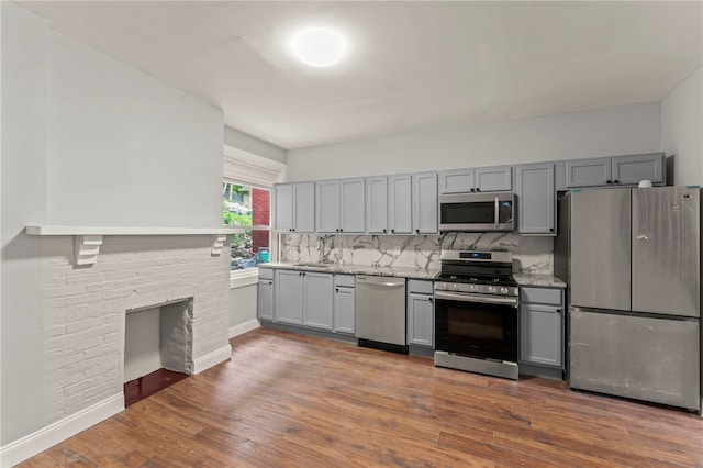 kitchen with gray cabinets, dark hardwood / wood-style floors, tasteful backsplash, light stone counters, and stainless steel appliances