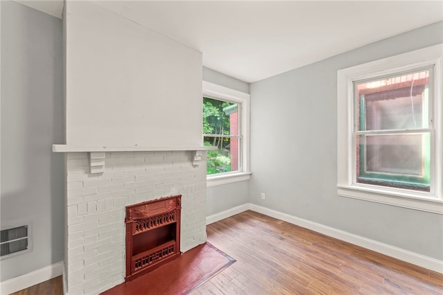 unfurnished living room with wood-type flooring and a brick fireplace