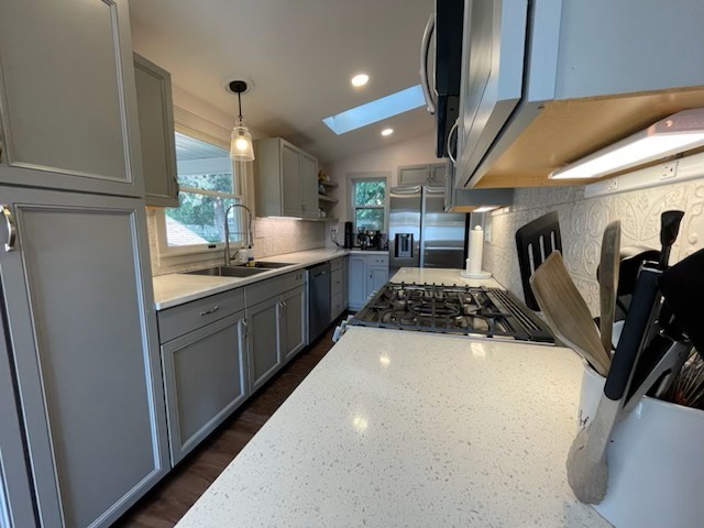 kitchen featuring sink, gray cabinetry, hanging light fixtures, lofted ceiling with skylight, and stainless steel appliances