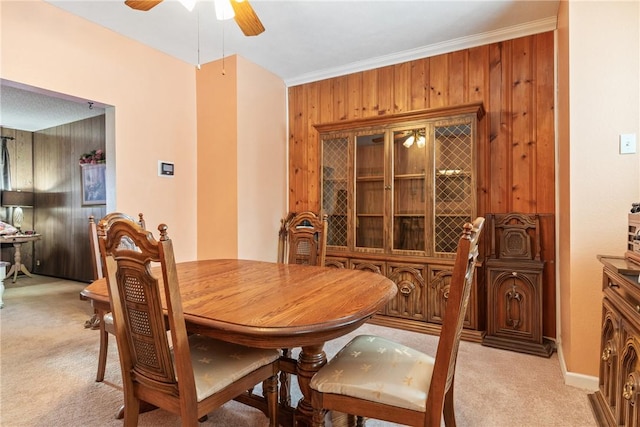 carpeted dining area featuring crown molding, wooden walls, and ceiling fan