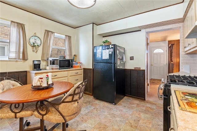 kitchen with ornamental molding, wall chimney range hood, wood walls, and black appliances