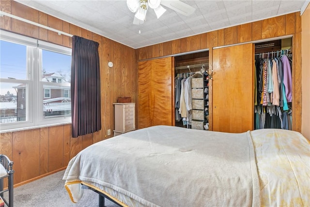 carpeted bedroom featuring ceiling fan and wood walls