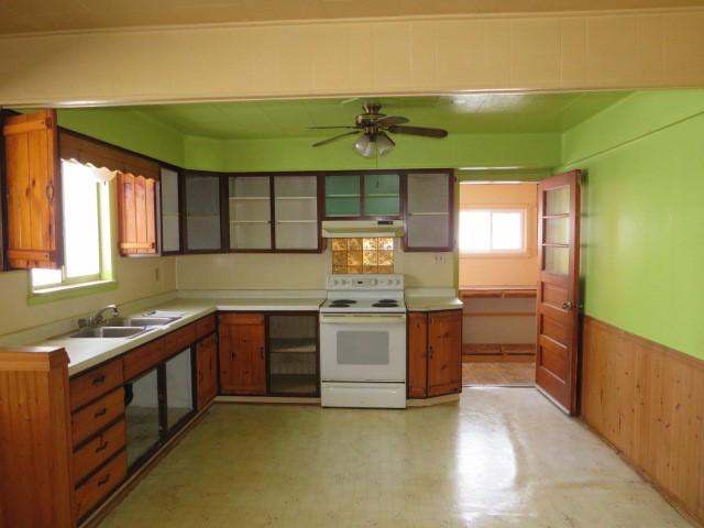 kitchen with ceiling fan, sink, white electric range oven, and wooden walls