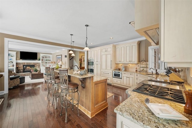 kitchen featuring a breakfast bar area, hanging light fixtures, a center island, light stone counters, and cream cabinetry