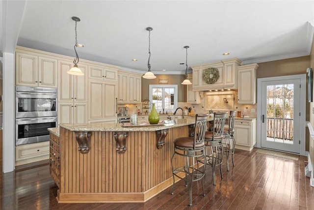 kitchen with a large island, pendant lighting, a breakfast bar, cream cabinetry, and stainless steel double oven