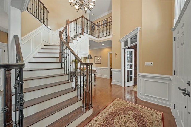 foyer entrance featuring a notable chandelier, a towering ceiling, dark wood-type flooring, and ornamental molding