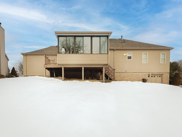 snow covered house with a wooden deck and a sunroom