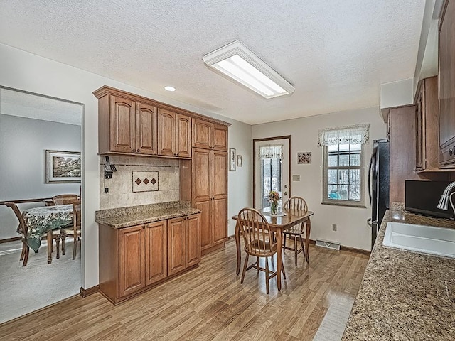 kitchen with black refrigerator, sink, decorative backsplash, a textured ceiling, and light wood-type flooring