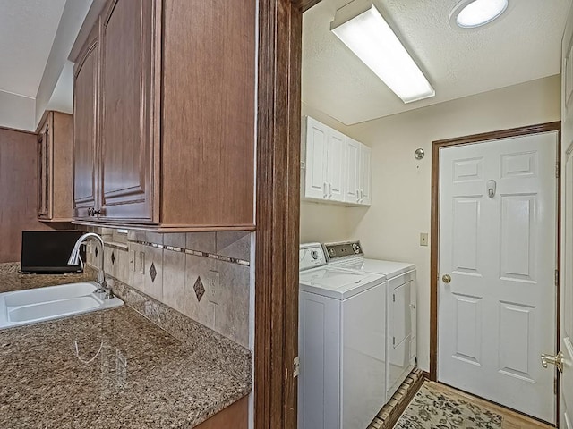 clothes washing area featuring sink, washing machine and dryer, and cabinets