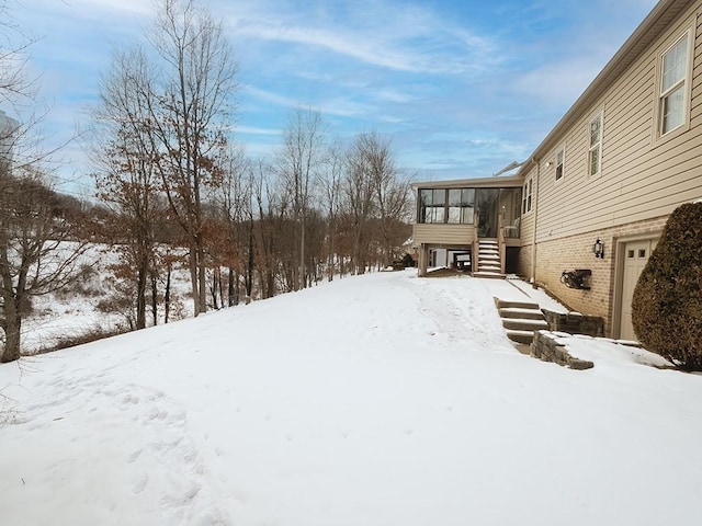 yard layered in snow with a garage and a sunroom