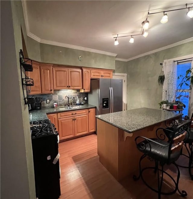 kitchen with stainless steel refrigerator with ice dispenser, sink, a breakfast bar area, light hardwood / wood-style floors, and black gas range