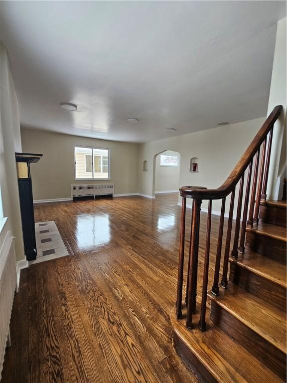 1732 Pennsylvania Ave, West Mifflin, PA 15122 - unfurnished living room featuring radiator heating unit, wood finished floors, arched walkways, baseboards, and stairway
